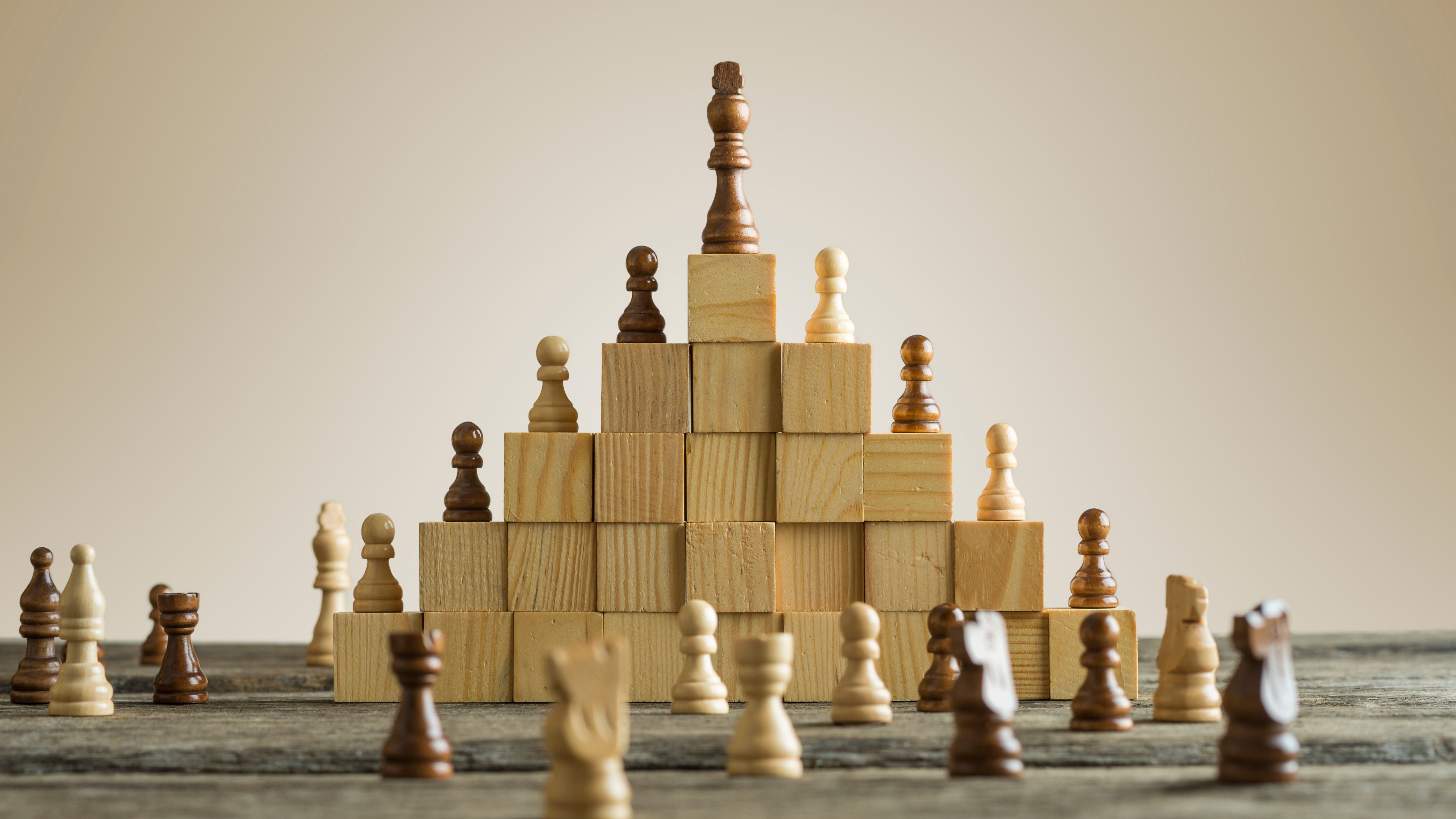 An image of blocks stacked into a pyramid with a queen chess piece at the peak and pawns below (representing the academic hierarchy).